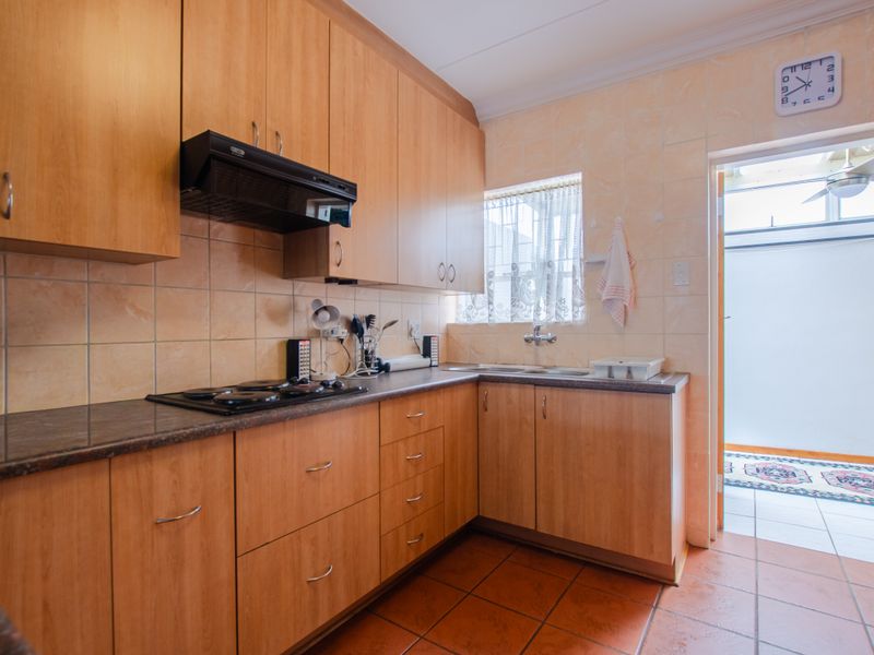 A functional kitchen featuring wood-look laminate cabinetry, a built-in electric hob with extractor fan, tiled splashbacks, and direct access to an outdoor area.