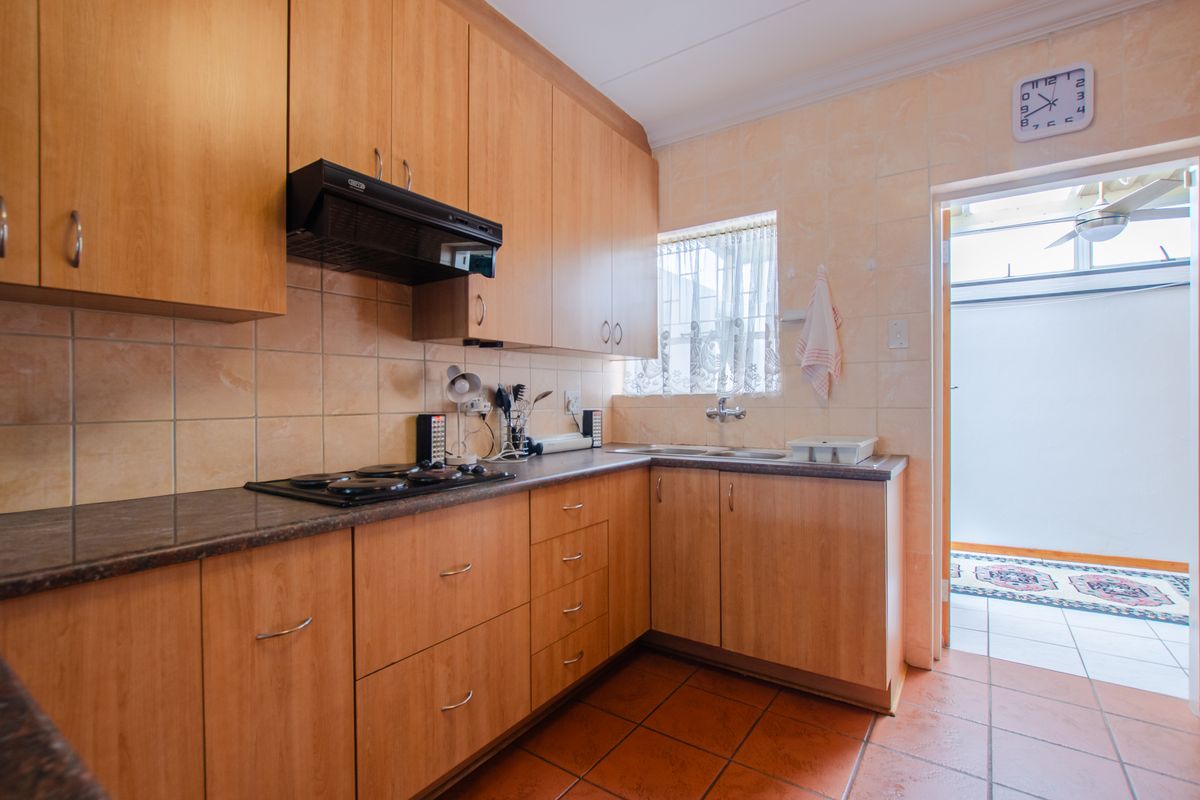 A functional kitchen featuring wood-look laminate cabinetry, a built-in electric hob with extractor fan, tiled splashbacks, and direct access to an outdoor area.