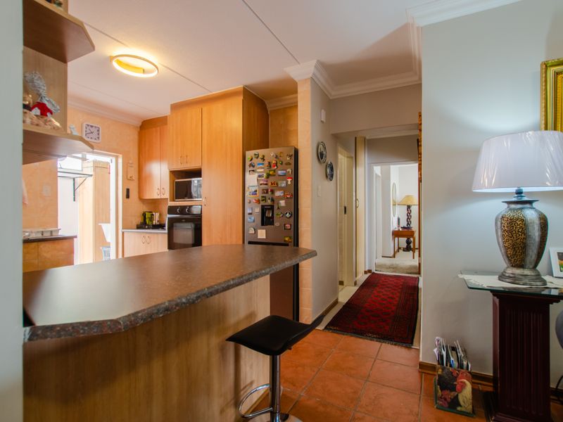 Open plan kitchen area featuring wooden cabinetry, laminate countertops, and built-in appliances, flowing into a tiled hallway space.
