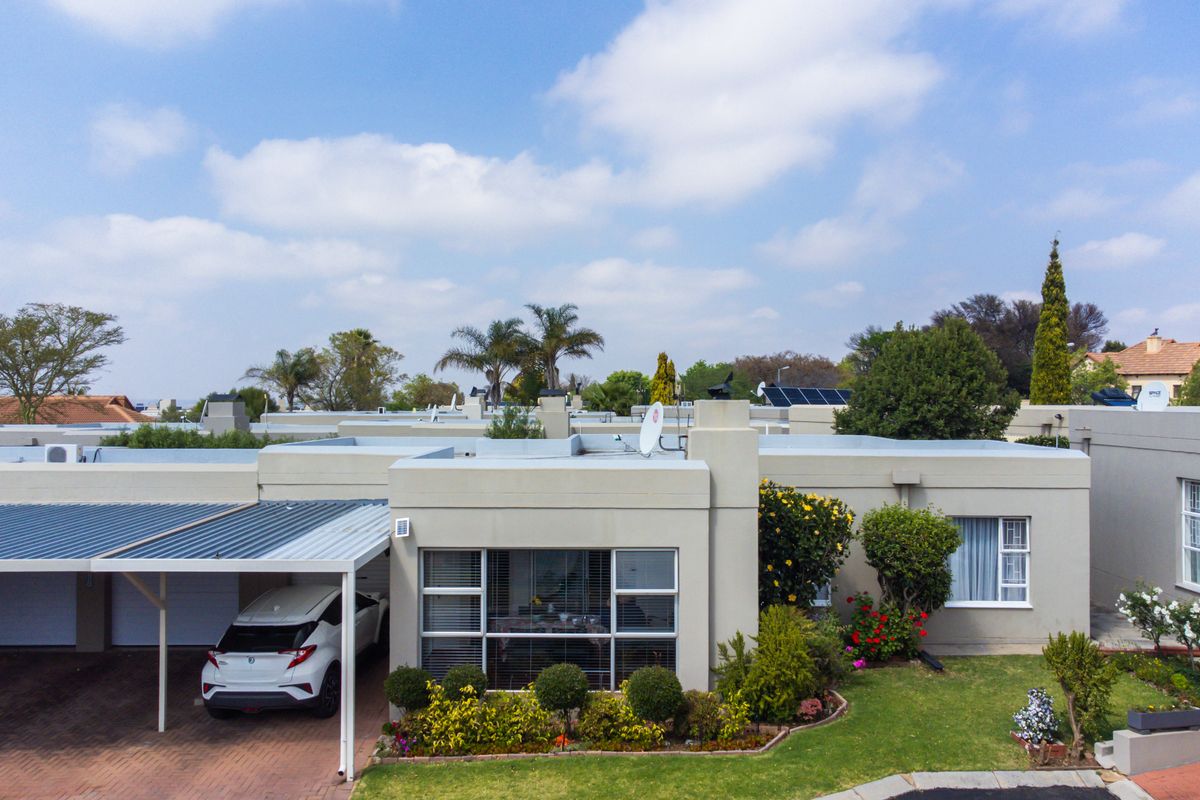 Aerial view of a townhouse complex featuring a paved driveway, carport, flat roof architecture, and a well-maintained front garden.