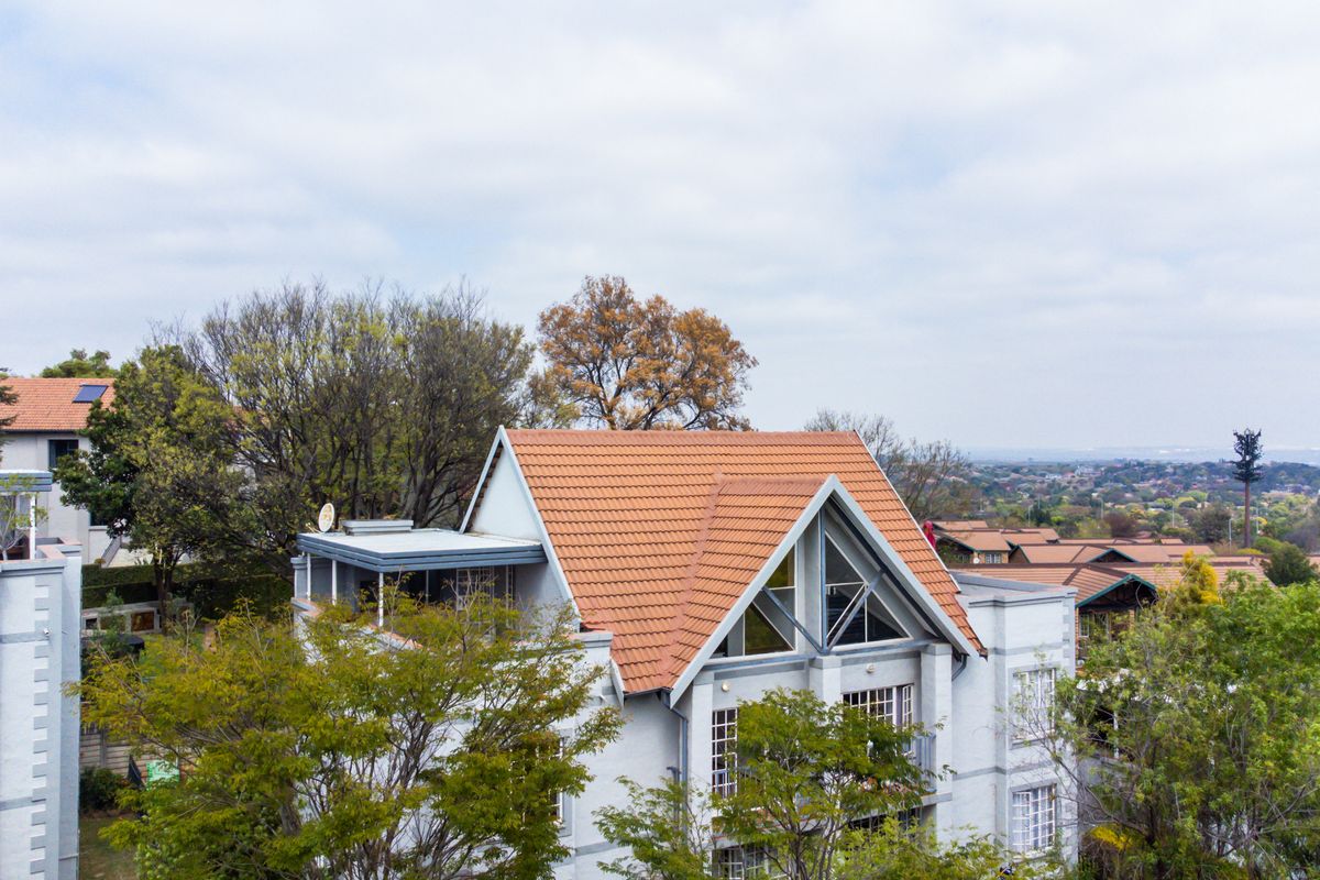 Aerial view of an apartment complex featuring pitched terracotta tiled roofs, gable windows, and surrounding mature trees in a residential setting.