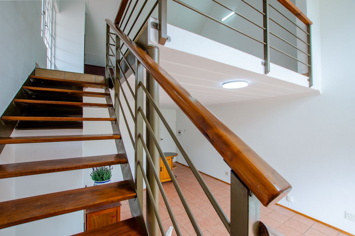 Open plan living area featuring a staircase leading to a mezzanine level with metal balustrades and tiled flooring.
