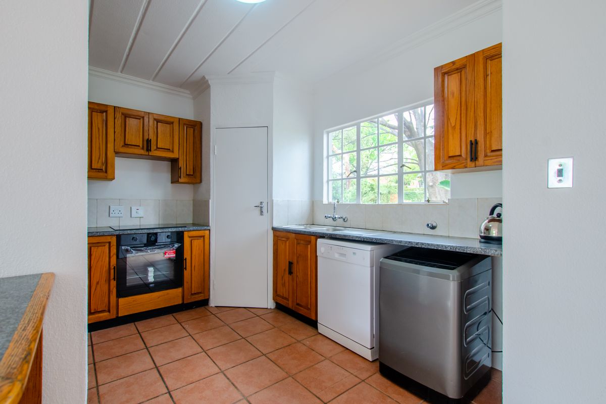 A functional kitchen featuring wooden cabinetry, built-in oven, hob, double sink, and tiled flooring with ample natural light from the window.