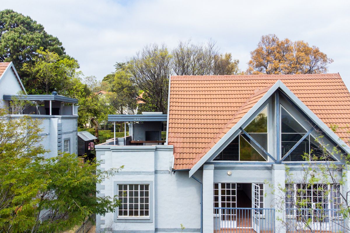 Rear exterior view of a multi-level apartment building featuring terracotta roof tiles, gabled architecture with large triangular windows, and a private balcony.