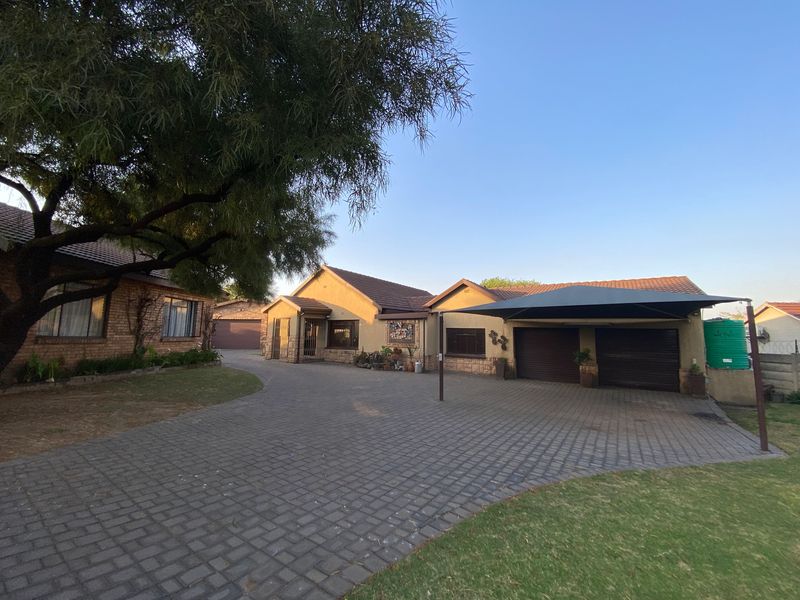 Front view of a residential property featuring a spacious paved driveway, double garage, carport, and established garden area.