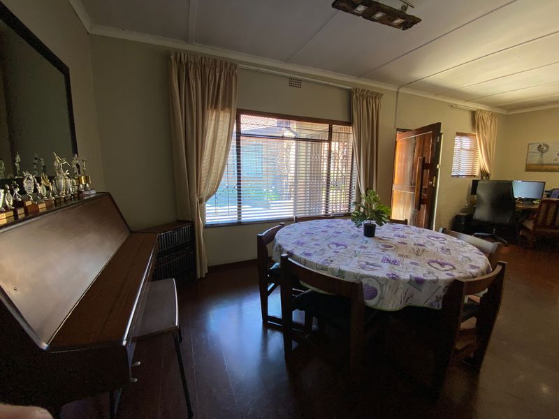 A dining room featuring laminate flooring, natural light through venetian blinds, and direct access to an adjacent workspace area.
