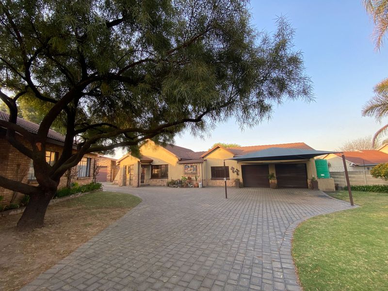 Front view of a residential property featuring a paved driveway, double garage with carport, and established garden with mature trees.