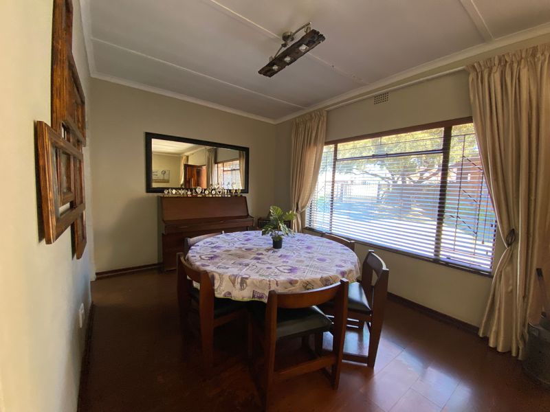 A functional dining room featuring laminate flooring, a large window with security bars, and neutral wall tones, offering a comfortable space for family meals.