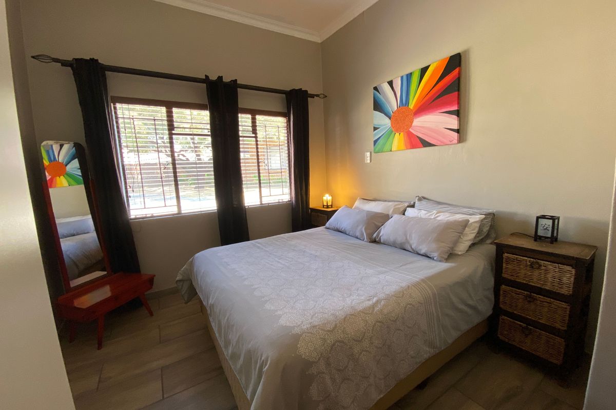 A cozy bedroom featuring tiled flooring, a window with security bars, and neutral wall tones, providing a comfortable and functional sleeping space.