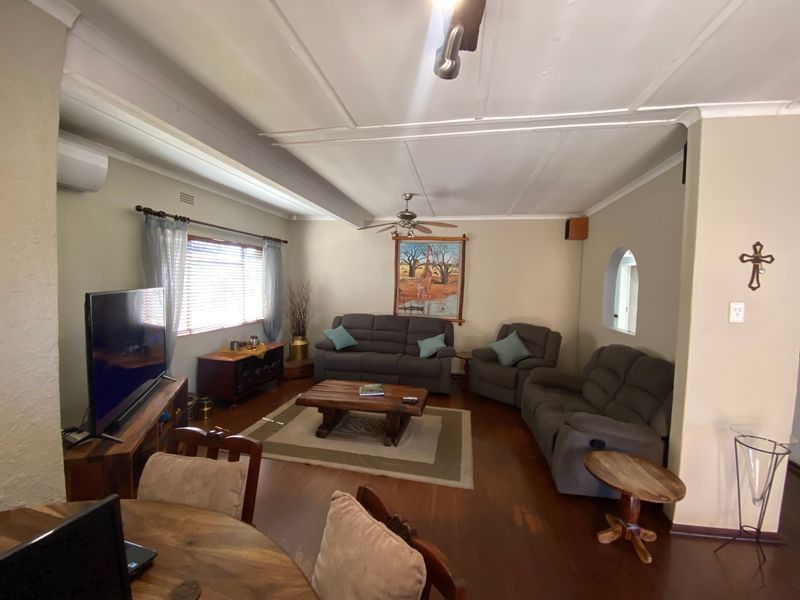 A spacious living room featuring timber flooring, a ceiling fan, and a split-system air conditioner, with an arched opening leading to adjacent areas.