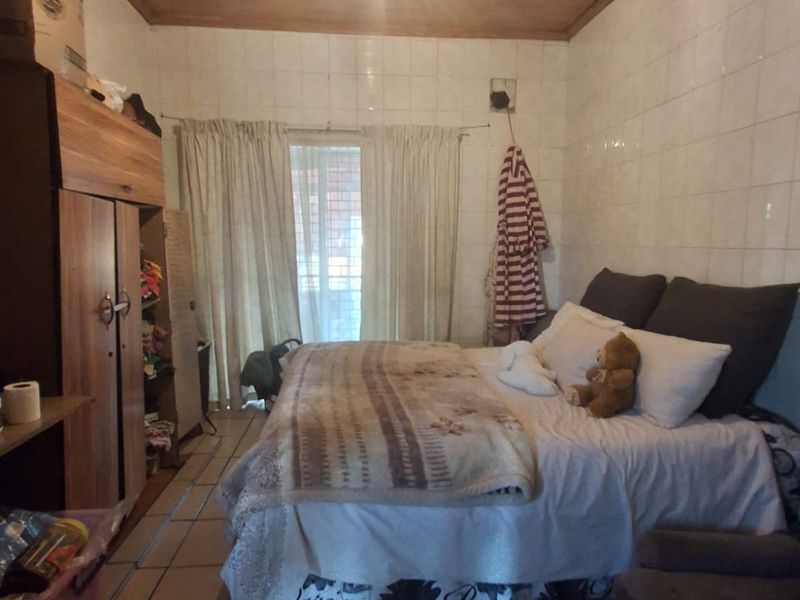 A bedroom featuring tiled flooring, fully tiled walls, and a timber-clad ceiling, offering a dated aesthetic ready for modernization.