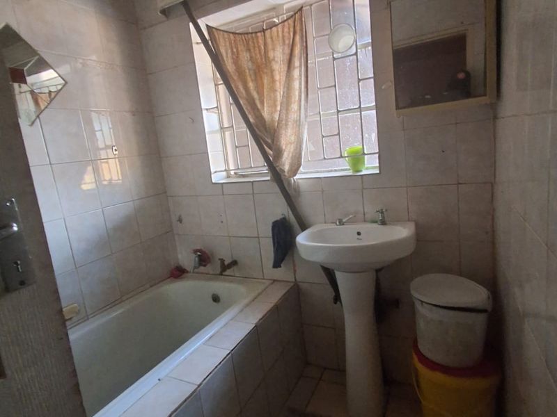 A dated bathroom featuring a built-in bathtub, pedestal basin, and tiled finishes, requiring significant renovation and modernization to improve functionality and aesthetic appeal.
