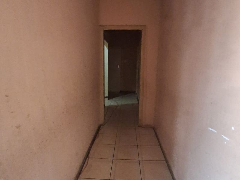 A narrow, empty hallway featuring tiled flooring and plain walls, currently showing signs of wear and requiring cosmetic updates.