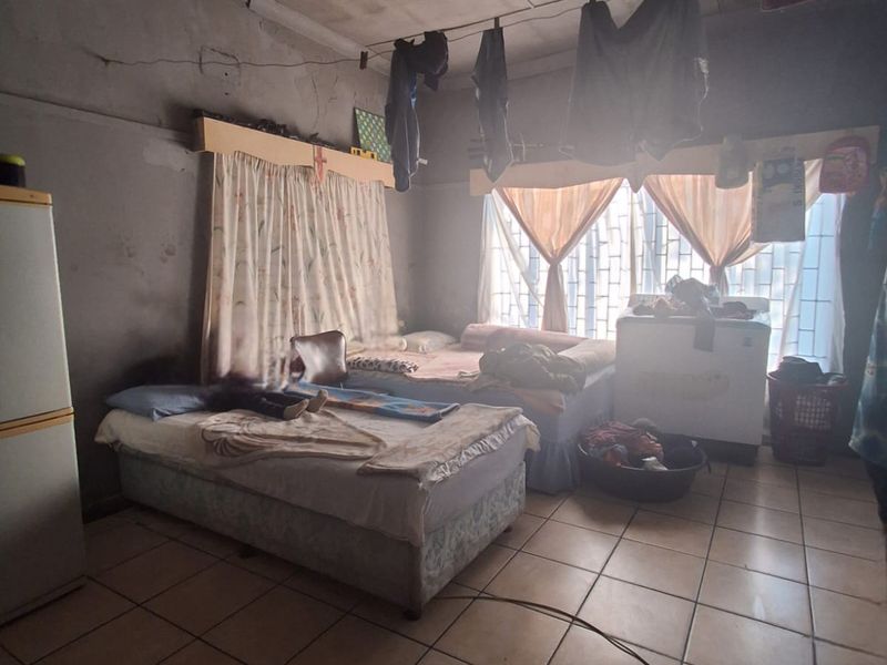 A bedroom featuring tiled flooring, a ceiling fan, and security bars on the windows, currently showing significant signs of wear and maintenance requirements.