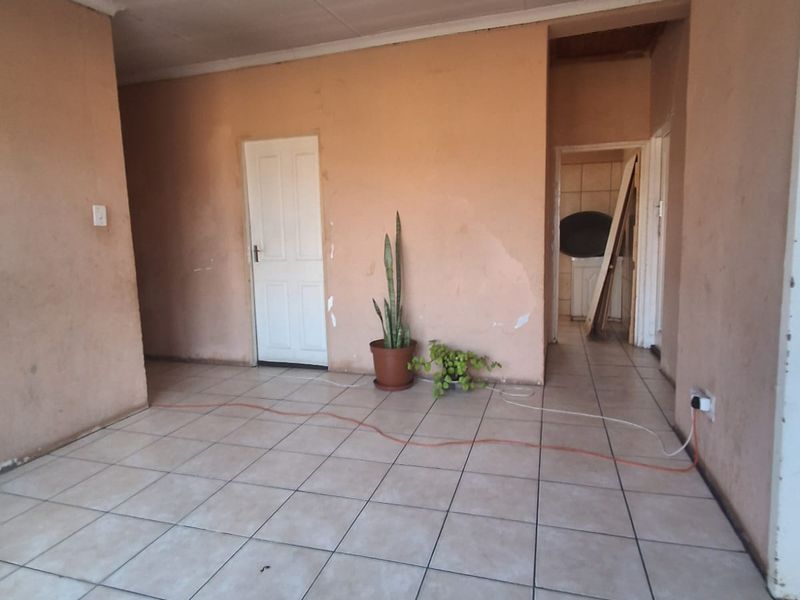 An empty living area featuring tiled flooring and plain walls, currently requiring ceiling and wall repairs to restore the space.