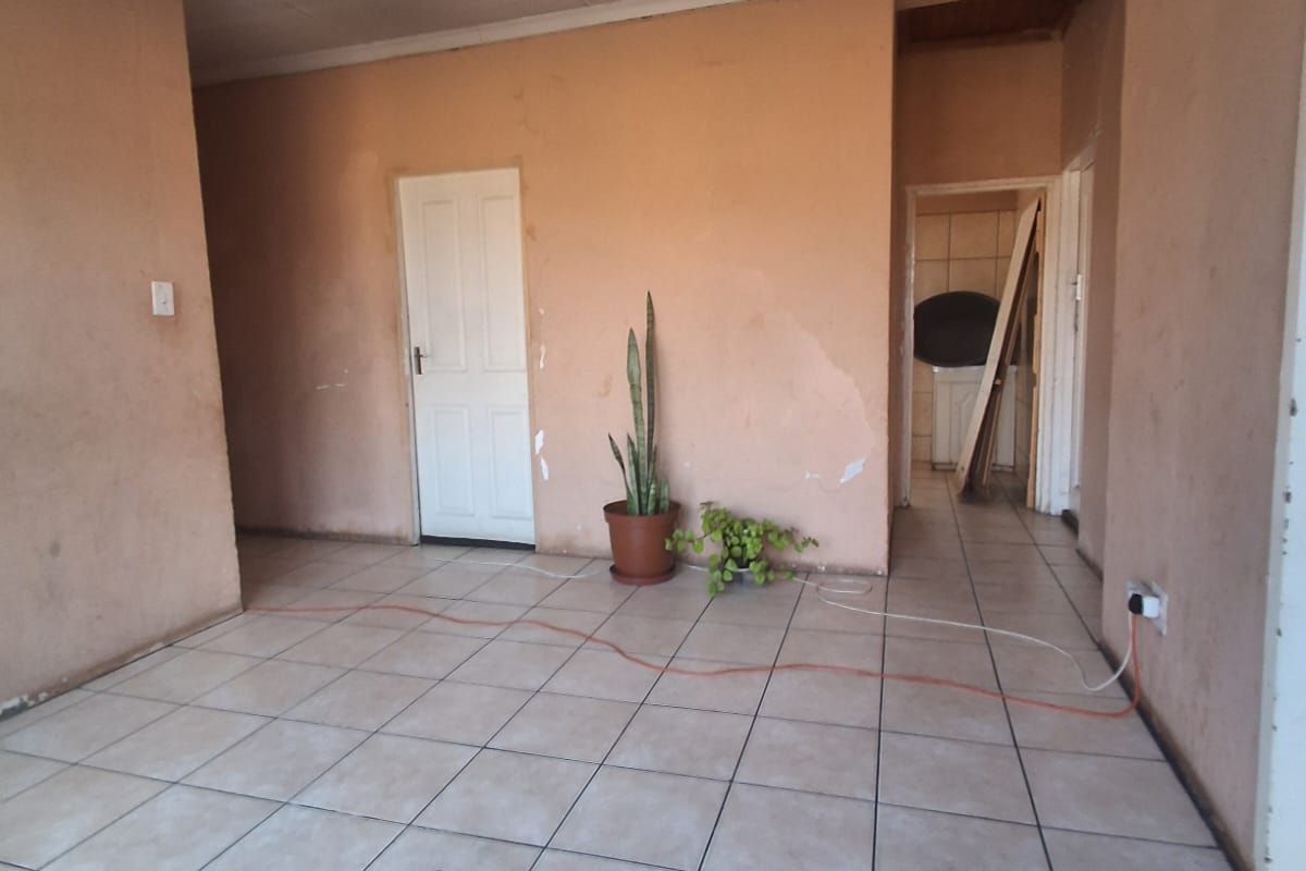 An empty living area featuring tiled flooring and plain walls, currently requiring ceiling and wall repairs to restore the space.