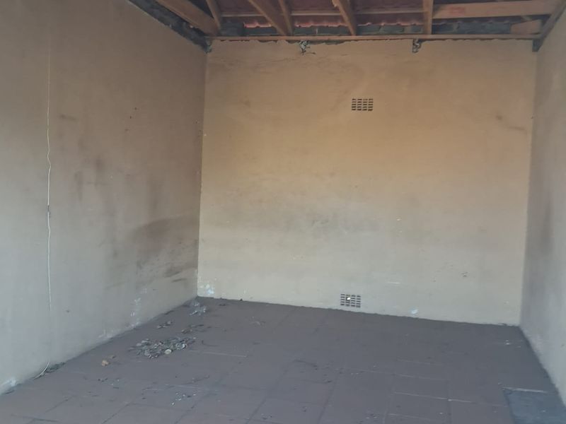 An unfinished garage space featuring exposed timber roof trusses, tiled flooring, and ventilation bricks, requiring completion and cosmetic repairs.