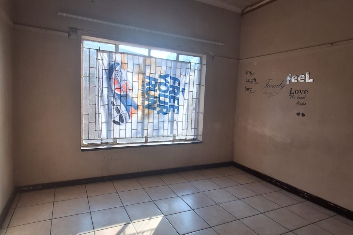 An empty bedroom featuring tiled flooring and security bars on the window, requiring cosmetic updates and wall repairs.