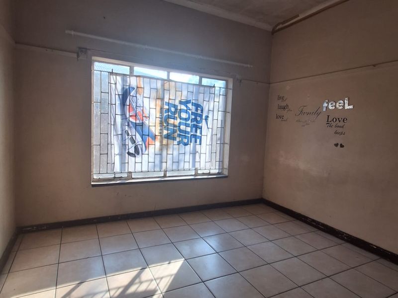 An empty bedroom featuring tiled flooring and security bars on the window, requiring cosmetic updates and wall repairs.
