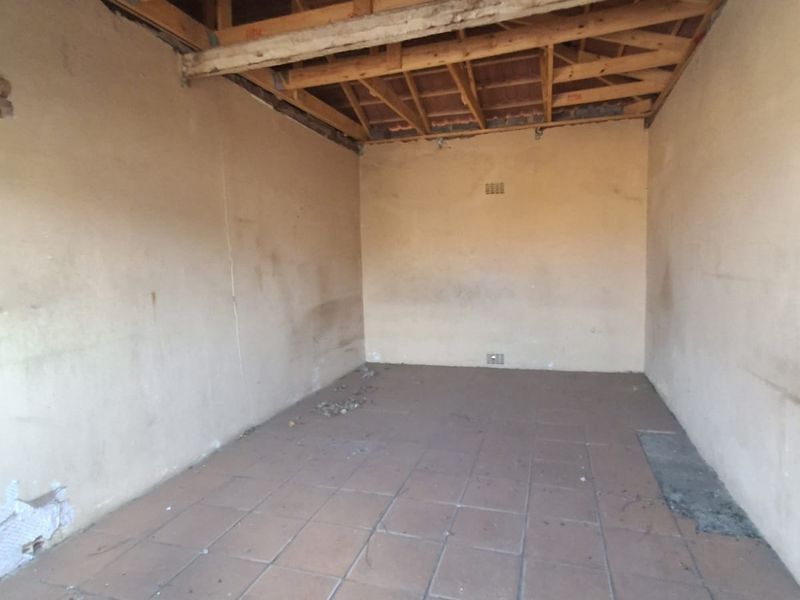An unfinished garage space featuring exposed timber roof trusses, tiled flooring, and ventilation bricks, requiring renovation to complete the interior finishes.