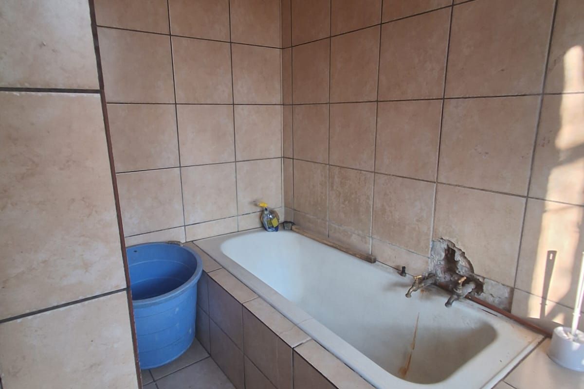 A dated bathroom featuring a built-in bathtub with tiled surround, requiring maintenance and repairs to the wall tiling and plumbing fixtures.