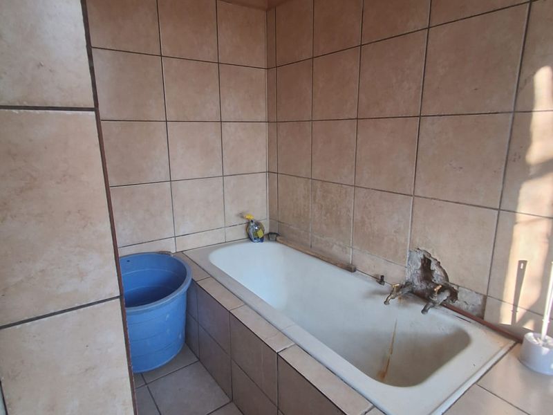 A dated bathroom featuring a built-in bathtub with tiled surround, requiring maintenance and repairs to the wall tiling and plumbing fixtures.