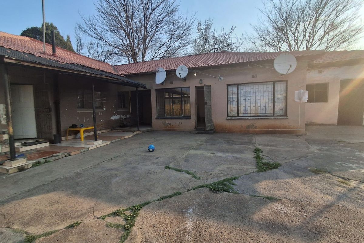 Rear exterior view of the house featuring a concrete patio area, tiled roof, and security bars on the windows.
