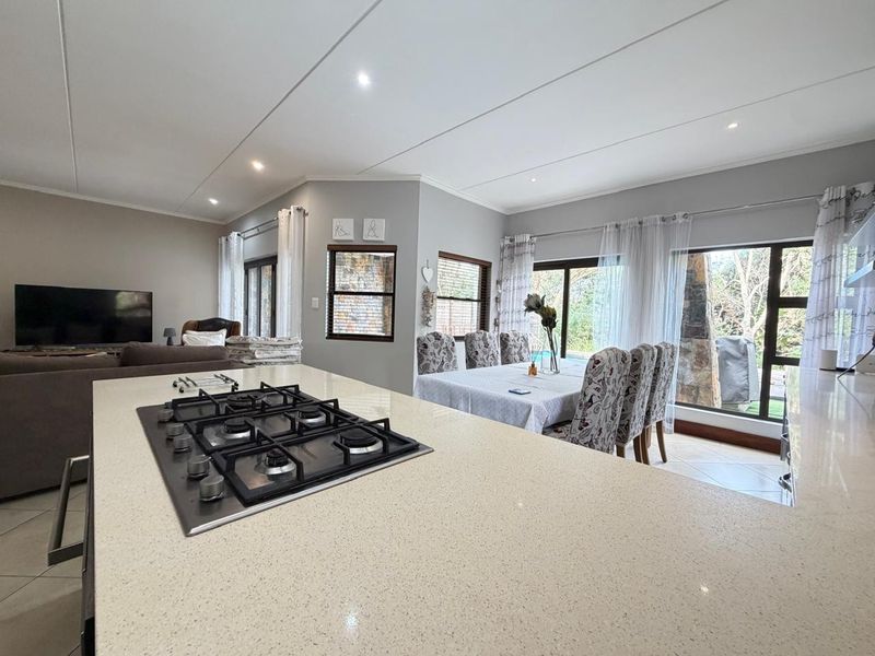 Spacious open-plan living and dining area featuring a modern kitchen island with a built-in gas hob, tiled floors, and large sliding doors to the garden.