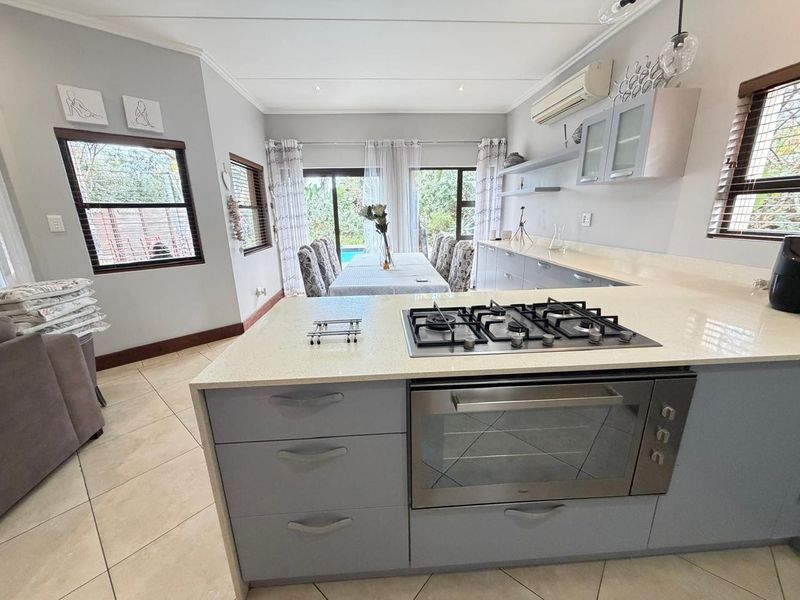 Open-plan kitchen and dining area featuring a central island with gas cooktop, stone countertops, and direct access to the outdoor patio area.