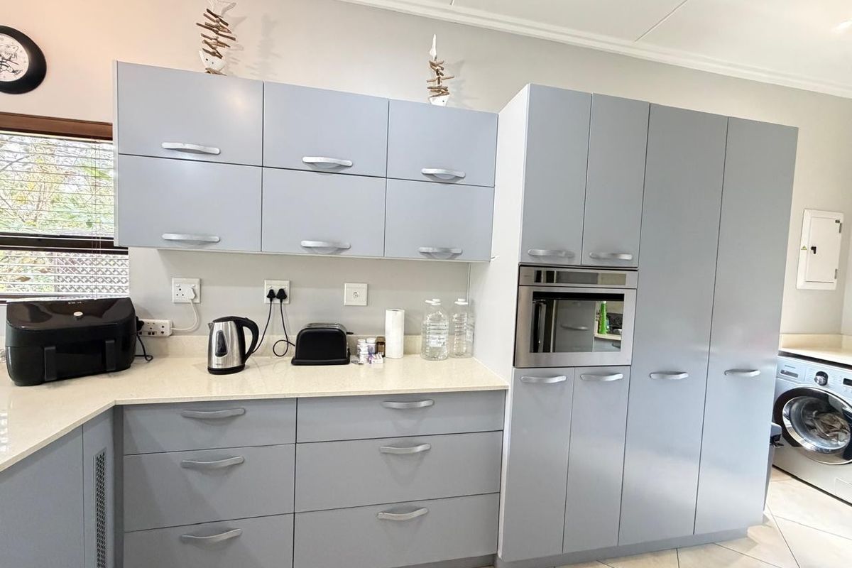 A modern kitchen featuring light grey cabinetry, stone countertops, a built-in oven, and an integrated laundry space with tiled flooring.