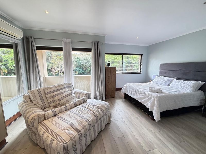 Spacious bedroom featuring light-toned tiled flooring, recessed lighting, air conditioning, and direct access to a private balcony through sliding glass doors.