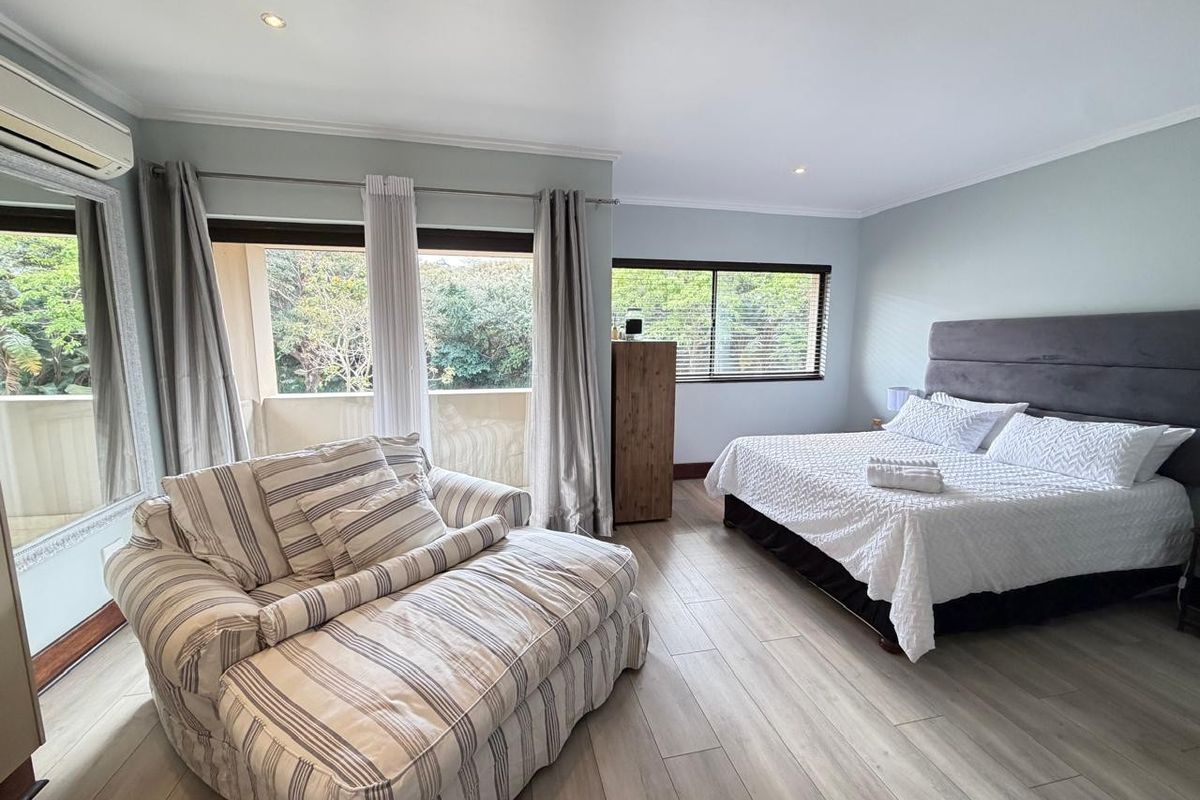 Spacious bedroom featuring light-toned tiled flooring, recessed lighting, air conditioning, and direct access to a private balcony through sliding glass doors.