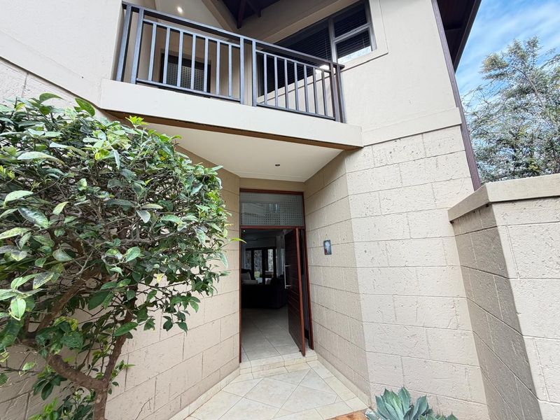 Entrance area of the townhouse featuring tiled flooring, a covered porch, and an upper-level balcony with metal railings.