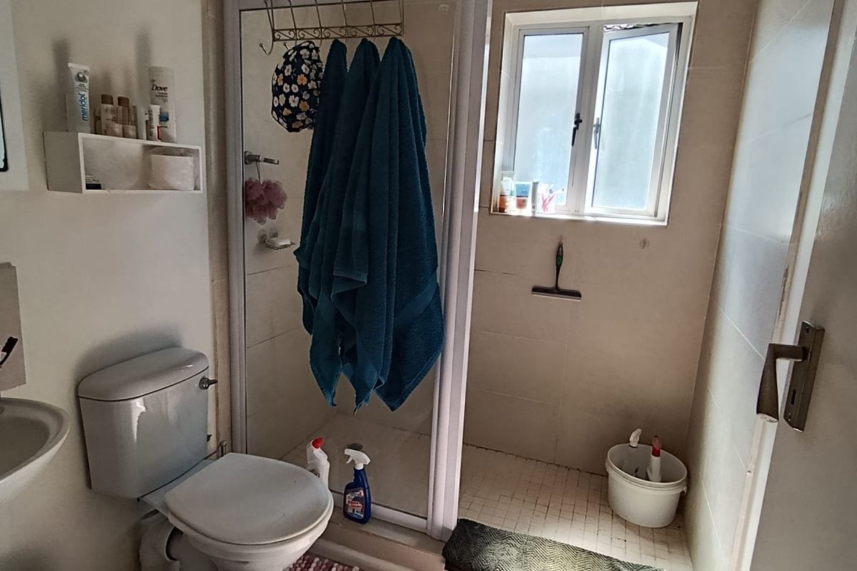 A functional bathroom featuring a shower enclosure, toilet, and washbasin with neutral wall and floor tiling.