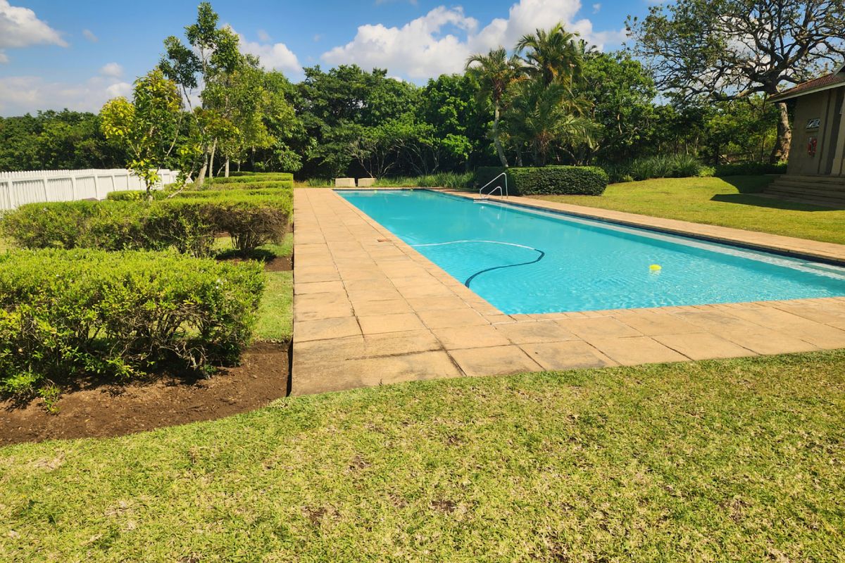 A well-maintained rectangular swimming pool set within a landscaped garden, featuring a paved surround and a white picket fence boundary.