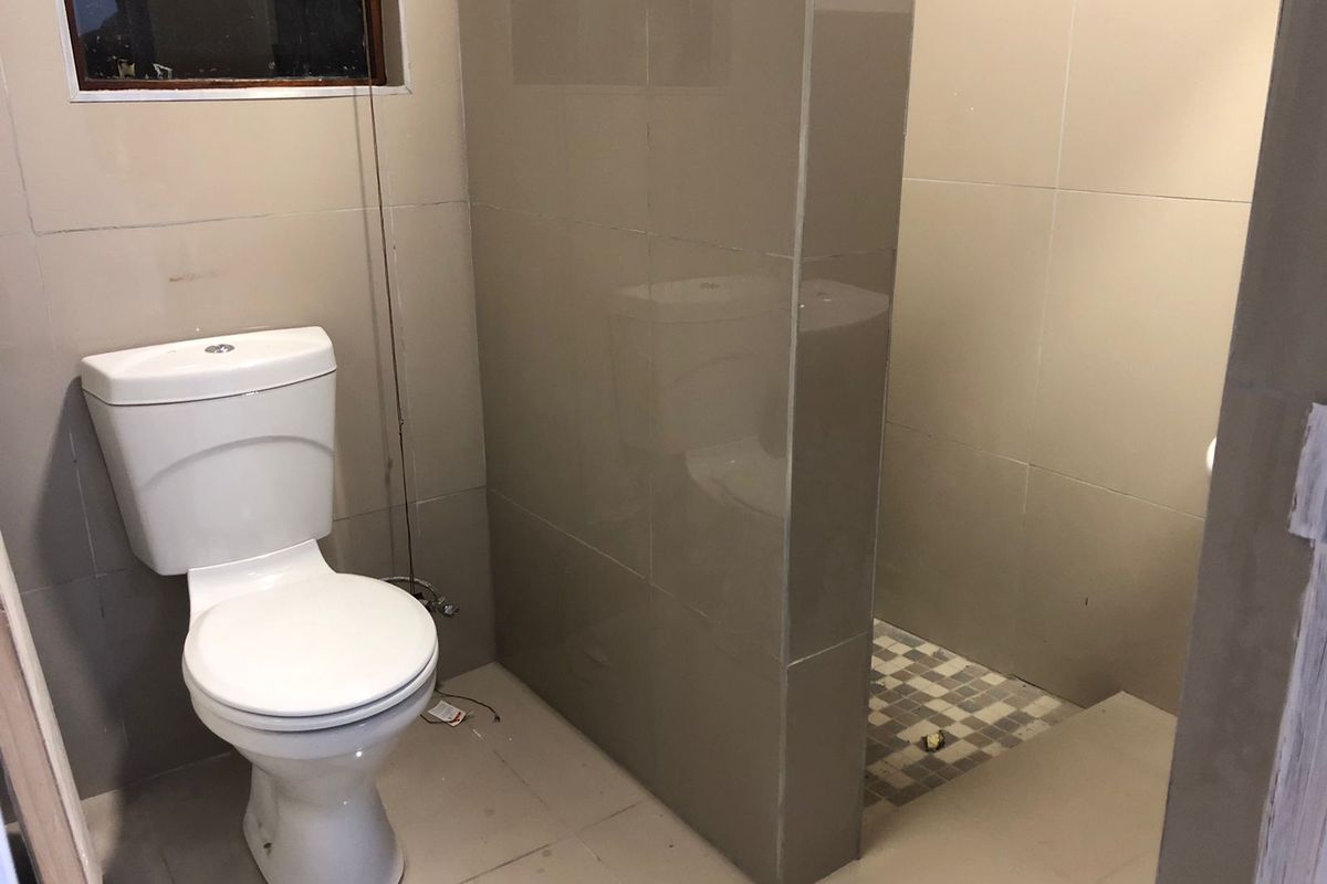 A compact bathroom featuring a toilet and a tiled shower area, currently in an unfinished state requiring cosmetic completion.