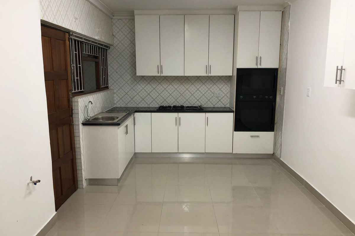 A clean, modern kitchen featuring white cabinetry, built-in oven, gas hob, and tiled finishes, offering a functional and bright workspace.