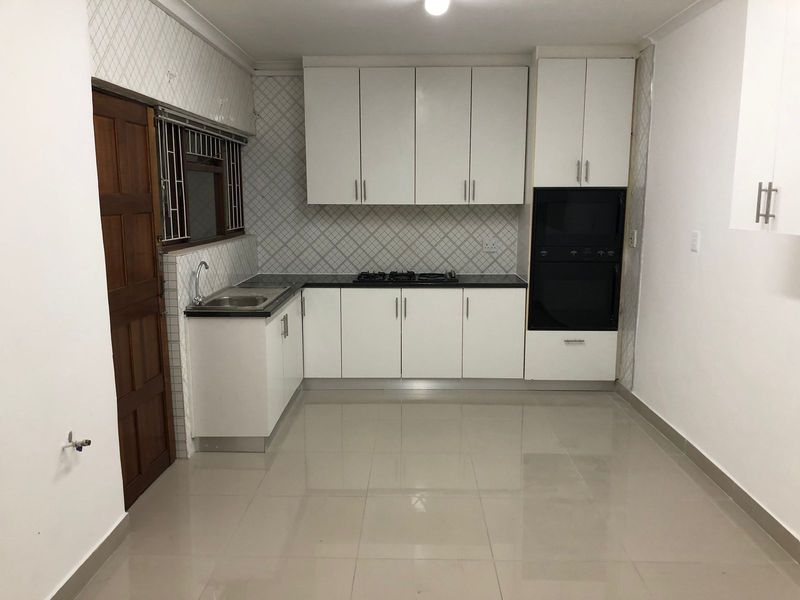 A clean, modern kitchen featuring white cabinetry, built-in oven, gas hob, and tiled finishes, offering a functional and bright workspace.