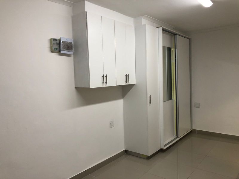 A clean, empty bedroom featuring neutral tiled flooring, built-in white cabinetry, and a large sliding wardrobe with a mirrored panel.