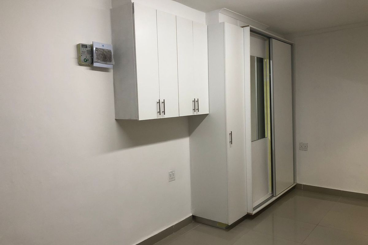 A clean, empty bedroom featuring neutral tiled flooring, built-in white cabinetry, and a large sliding wardrobe with a mirrored panel.