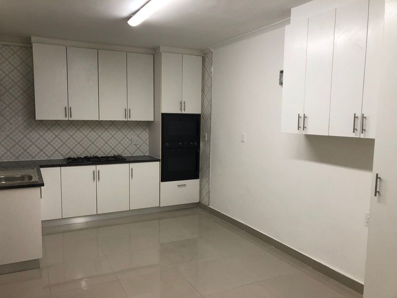 A clean, functional kitchen featuring white cabinetry, a built-in double oven, gas hob, tiled backsplash, and neutral floor tiles.
