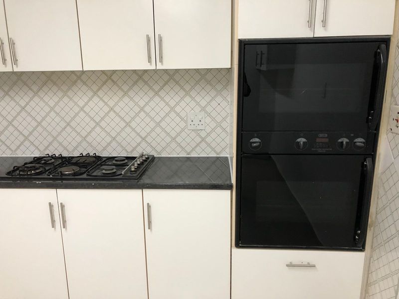 A functional kitchen area featuring white cabinetry, a built-in oven and microwave unit, a gas hob, and a diamond-patterned tiled backsplash.