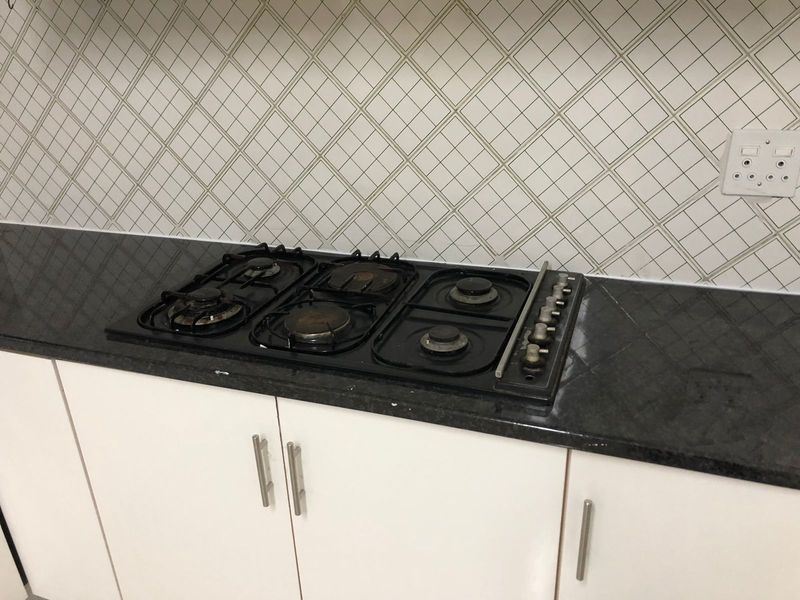 A kitchen workspace featuring a black gas cooktop set into a dark granite countertop with a white tiled backsplash and white cabinetry.