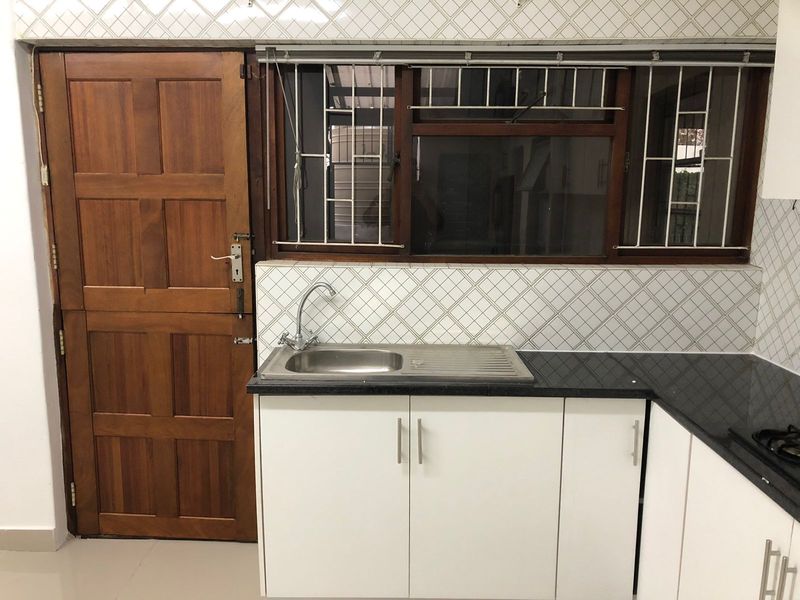 A functional kitchen area featuring white cabinetry, granite countertops, a stainless steel sink, and a wooden door with security bars on the window.