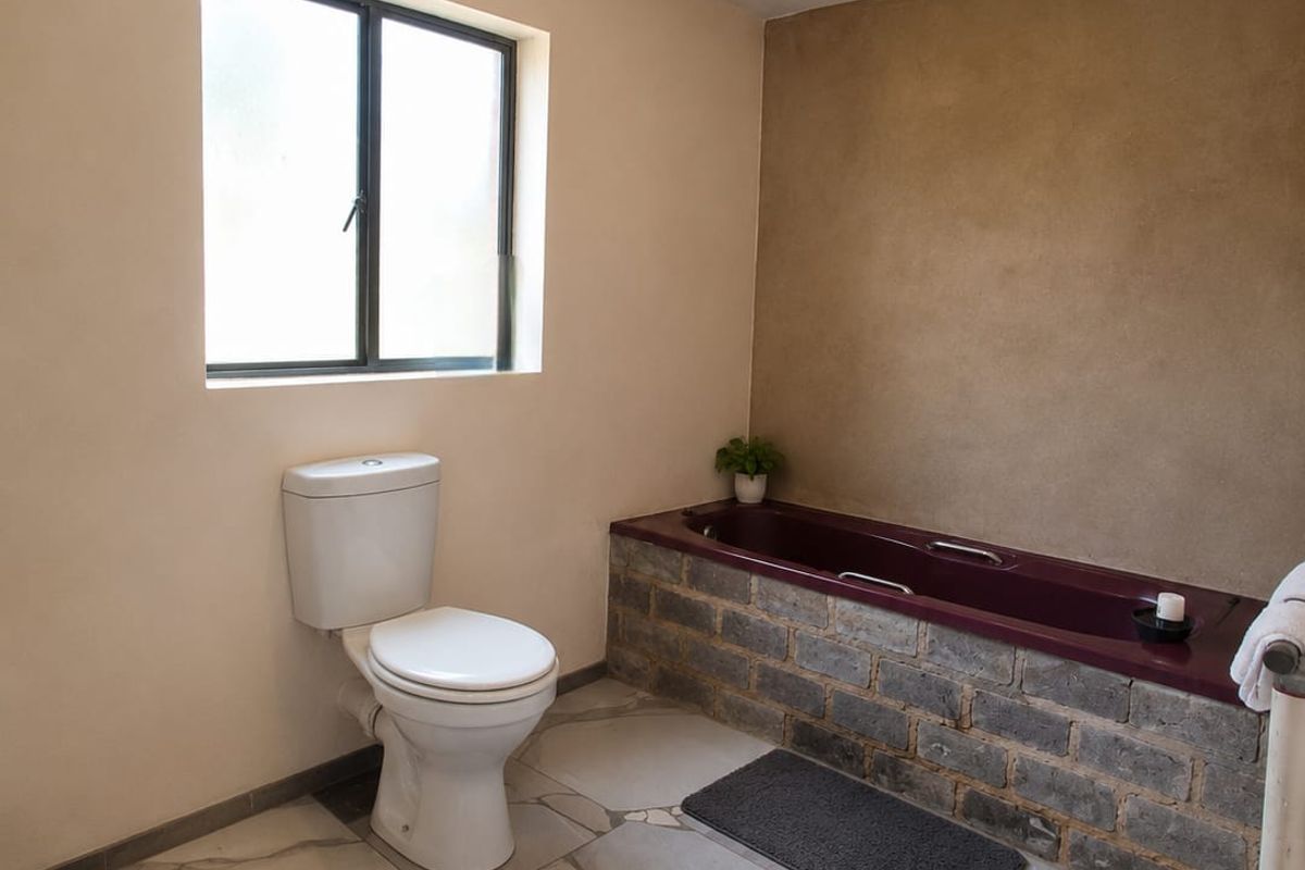 A bathroom featuring a toilet and a bathtub with a rustic brick-clad surround, finished with large-format floor tiles.