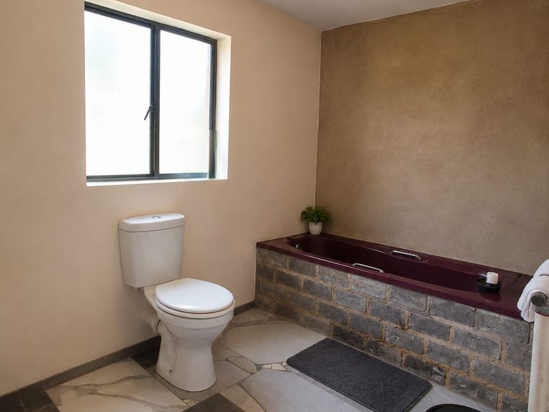 A bathroom featuring a toilet and a bathtub with a rustic brick-clad surround, finished with large-format floor tiles.