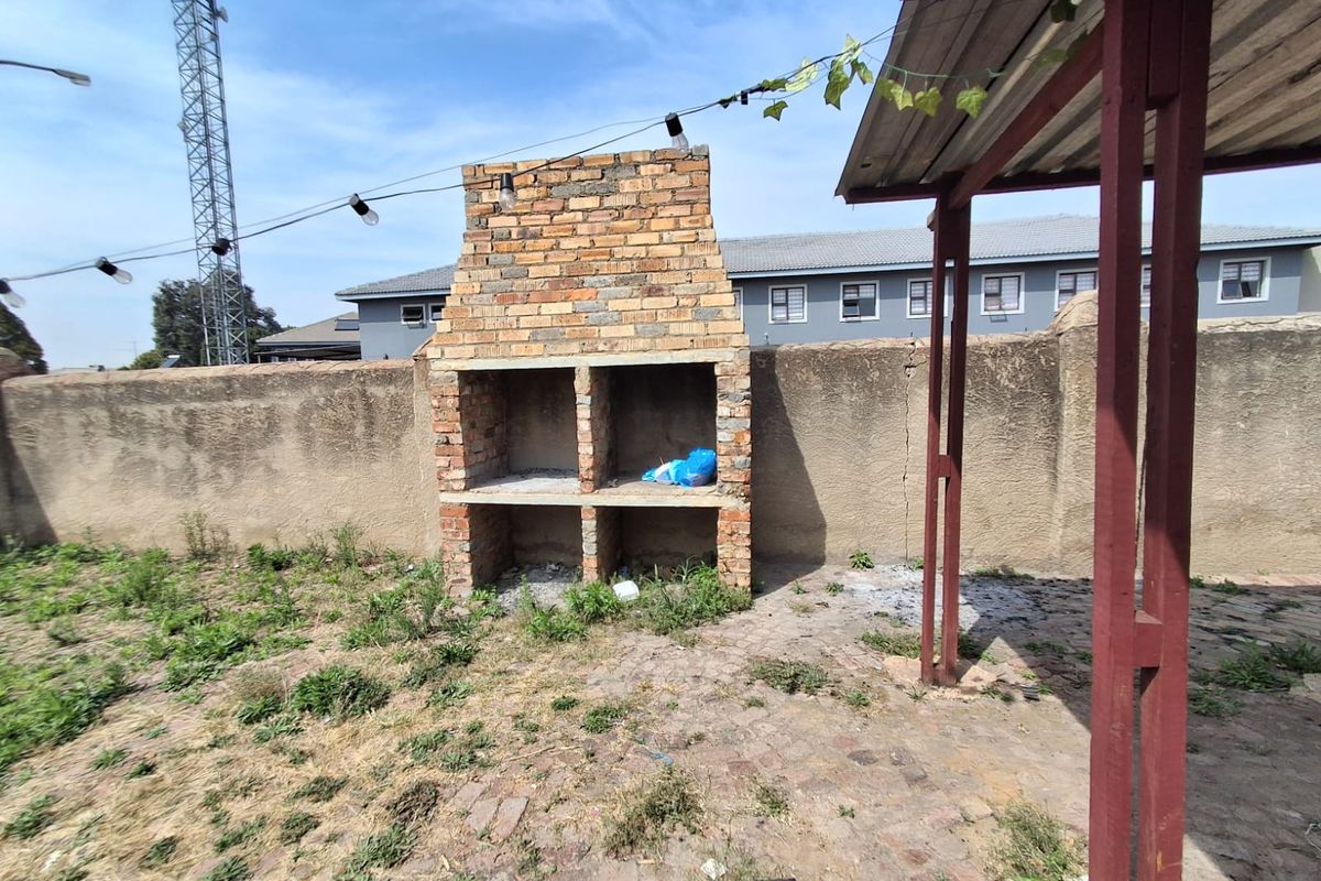 Outdoor patio area featuring a built-in brick braai, paved flooring, and a covered structure, requiring maintenance and landscaping to improve the space.