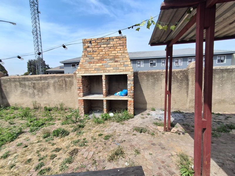 Outdoor patio area featuring a built-in brick braai, paved flooring, and a covered structure, requiring maintenance and landscaping to improve the space.