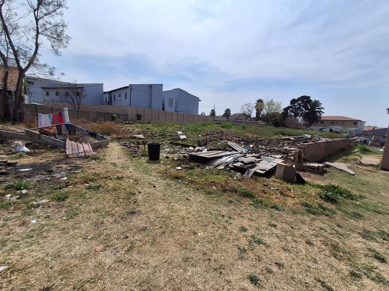 An undeveloped residential plot featuring perimeter walling and significant debris, requiring extensive clearing and landscaping to prepare for potential development.