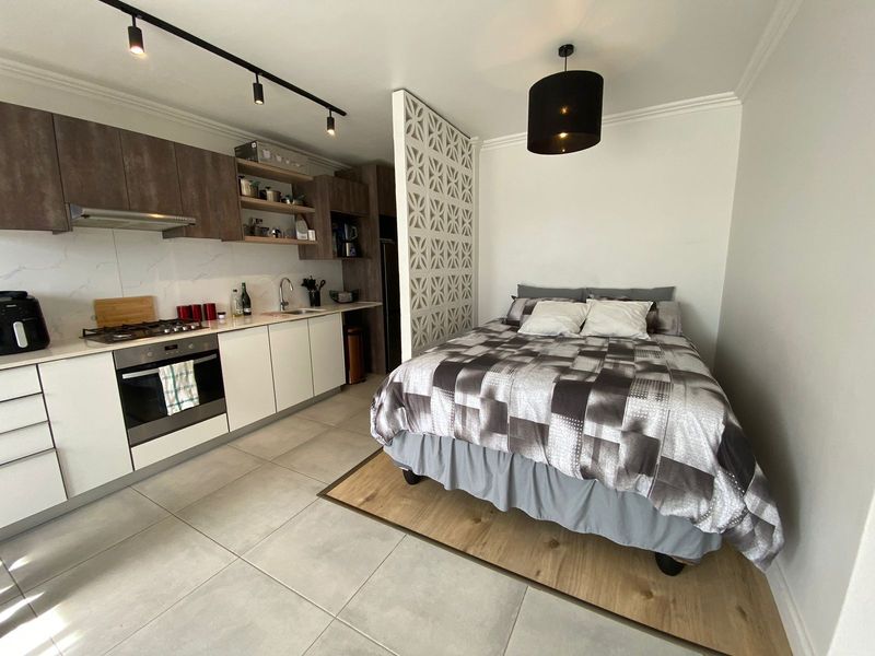 Modern open-plan studio apartment featuring a well-equipped kitchen with built-in appliances and a decorative partition separating the sleeping area.